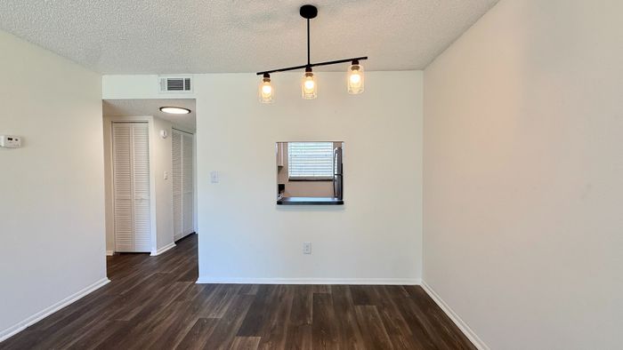 Inviting dining area with modern lighting and open pass-through to a bright kitchen, featuring elegant wooden flooring.