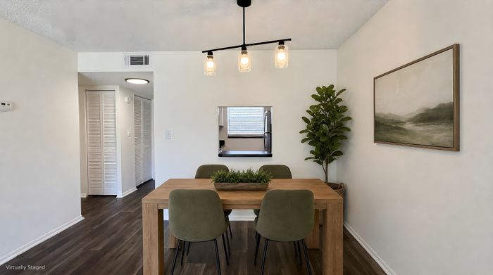 Chic dining area featuring modern lighting, a wooden table, and stylish green chairs, adjacent to a cozy kitchen, perfect for entertaining.