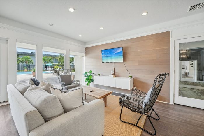 Bright, inviting living room with modern decor, large windows overlooking a beautiful outdoor pool area, and a stylish wooden accent wall.