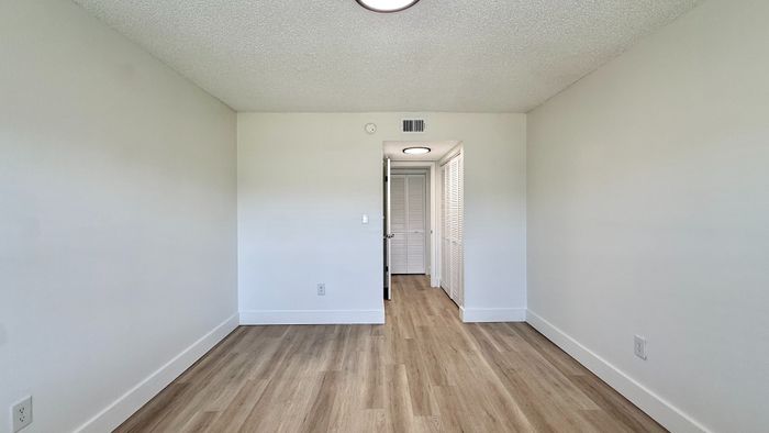 Bright empty room with modern wood flooring, white walls, and a closet, ideal for versatile living space.