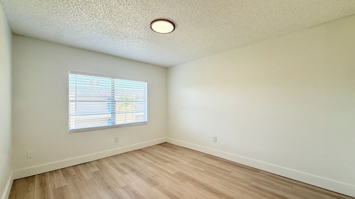 Sunlit, spacious room with clean white walls and elegant wood flooring, ideal for a cozy bedroom or modern office space.