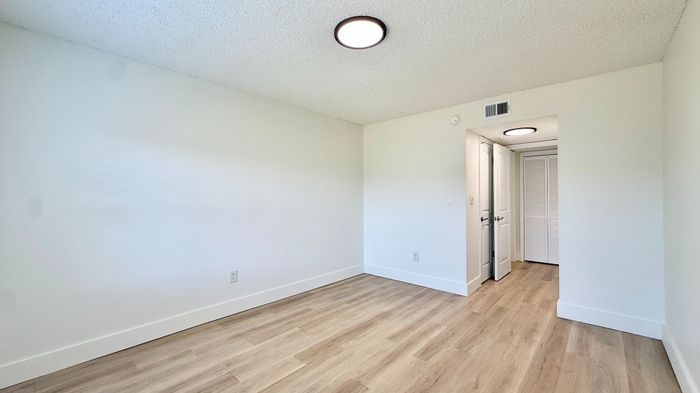 Bright and minimalist room with sleek wood flooring and modern ceiling light, perfect for customization and personal retreat.