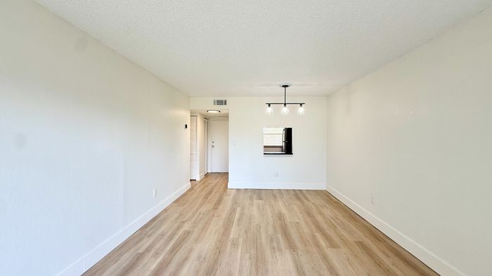 Bright, modern living area featuring elegant hardwood floors, minimalistic white walls, and stylish pendant lighting, perfect for a contemporary lifestyle.