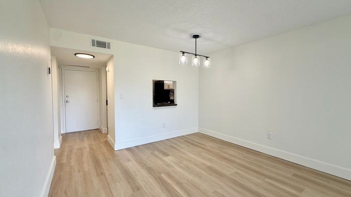 Contemporary apartment with elegant wood flooring, modern chandelier, and a cozy kitchen pass-through window.