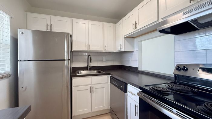 Modern kitchen with sleek stainless steel appliances, elegant white cabinetry, and a stylish black countertop, filled with natural light for a welcoming atmosphere.
