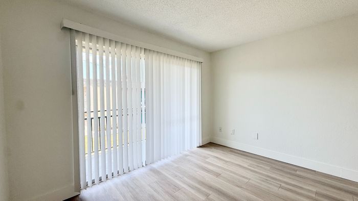 Bright apartment room with modern wood flooring and expansive sliding glass doors leading to a refreshing outdoor view.
