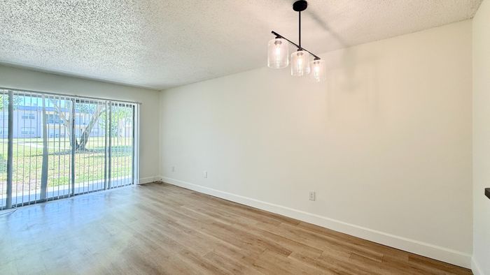 Bright and airy living room with elegant hardwood floors, modern chandelier, and large sliding glass doors overlooking a scenic view.