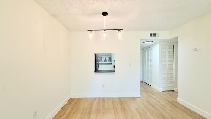 Bright dining area with elegant lighting and a passthrough window, featuring sleek hardwood floors and a modern open layout.