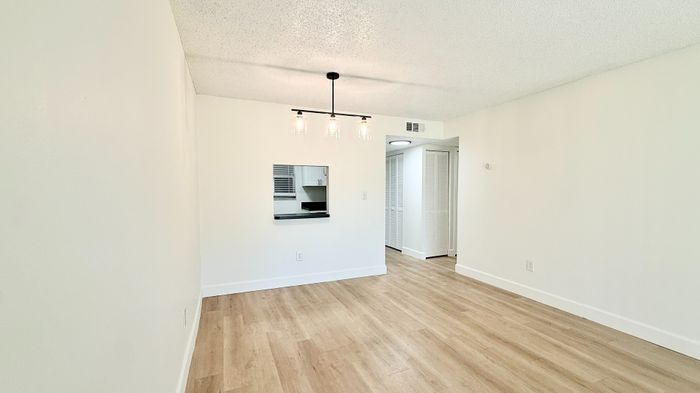Bright and modern apartment interior with sleek hardwood floors, elegant lighting, and a stylish pass-through window to the kitchen.