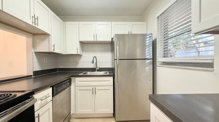 Modern kitchen with sleek stainless steel appliances, elegant white cabinetry, and a stylish dark countertop, complemented by natural light from a nearby window.