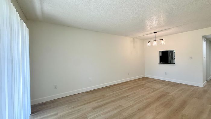 Bright and modern living area with sleek wood flooring, chic pendant lighting, and ample natural light from vertical blinds.