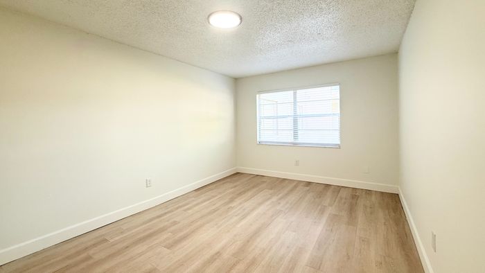 Bright and airy bedroom with large window, fresh white walls, and elegant wood flooring.