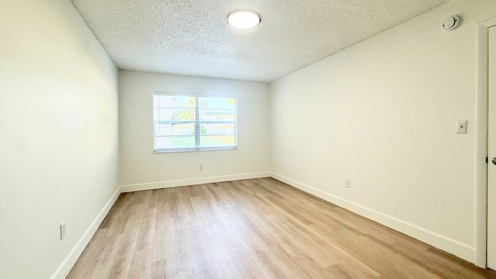 Bright and spacious bedroom with modern laminate flooring and a large window providing ample natural light.