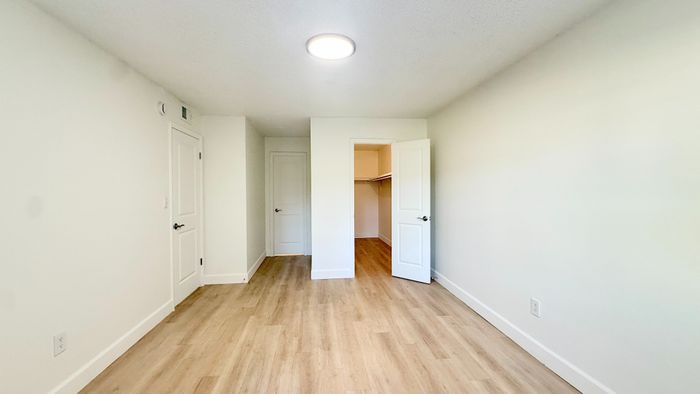 Bright and airy bedroom featuring sleek hardwood flooring, neutral walls, and a spacious walk-in closet.