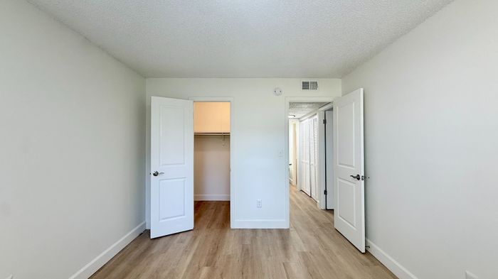 Chic bedroom space with clean white walls, elegant wooden flooring, and ample closet storage.