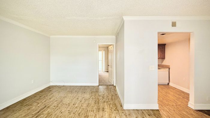 Inviting open-concept living area with sleek wood flooring and a glimpse into a modern kitchen with warm cabinetry.