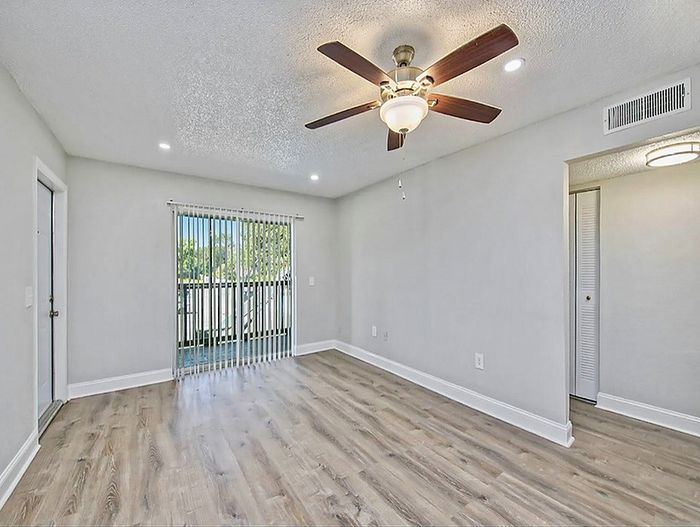 Bright and airy living room with modern ceiling fan and large sliding glass door leading to a serene balcony, perfect for relaxation.