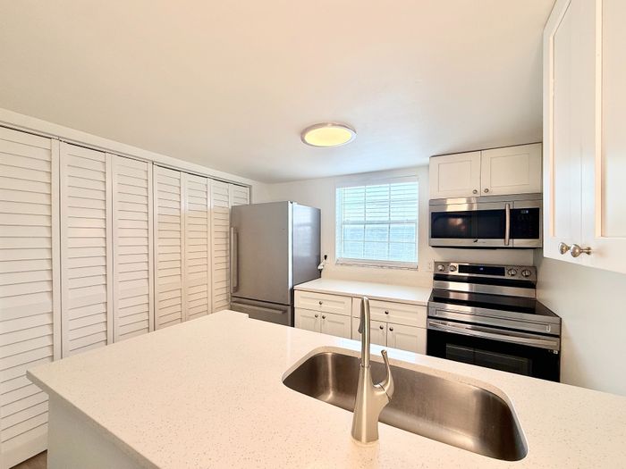 Bright, modern kitchen featuring sleek stainless steel appliances, elegant white cabinetry, and a spacious island with a stylish sink.