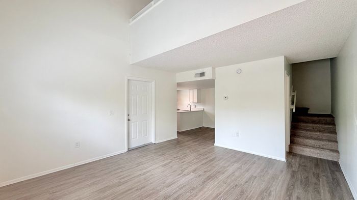 Bright and airy apartment interior featuring modern hardwood floors, a cozy open-plan kitchen, and carpeted stairs leading to a second level.
