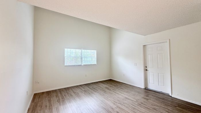 Bright and airy room with elegant wood flooring, freshly painted walls, and natural light streaming through a large window.