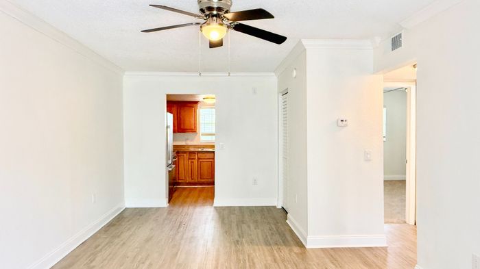 Bright, open living space with modern ceiling fan and sleek laminate flooring next to a cozy kitchen with warm wooden cabinetry.