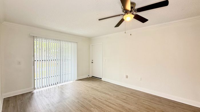 Bright living room featuring sleek hardwood floors, modern ceiling fan, and expansive sliding glass doors for natural light.