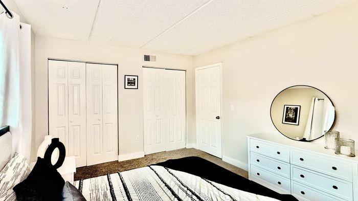 Bright, modern bedroom featuring dual closets, a sleek dresser with decorative accents, and soft, neutral tones.