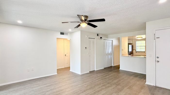Bright open-concept living space with elegant wood flooring and modern ceiling fan, leading to a sleek kitchen and ample storage.