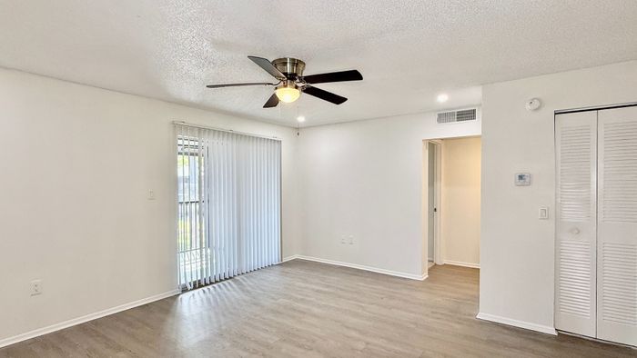 Bright and airy living space featuring modern ceiling fan, sleek floors, and sliding glass doors leading to a serene outdoor view.