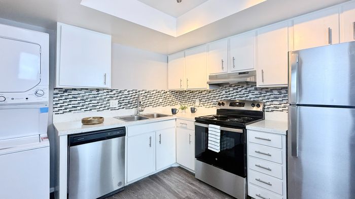 Modern kitchen with sleek stainless steel appliances, stylish mosaic backsplash, and an in-unit washer and dryer.