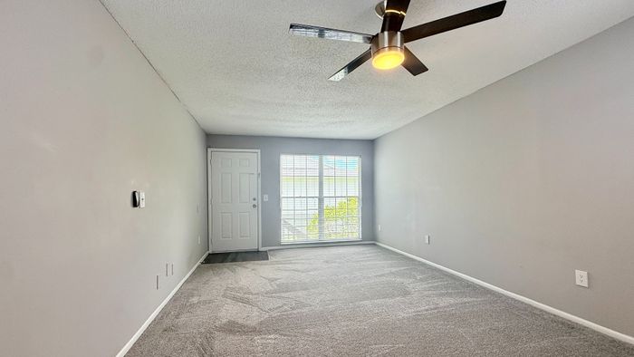 Inviting room with plush carpet, modern ceiling fan, and large sunlit window offering serene views.