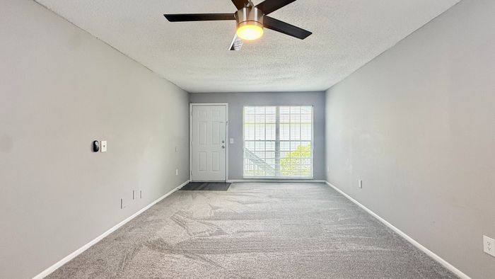 Bright and inviting living space with plush carpeting, modern ceiling fan, and large window offering natural light.