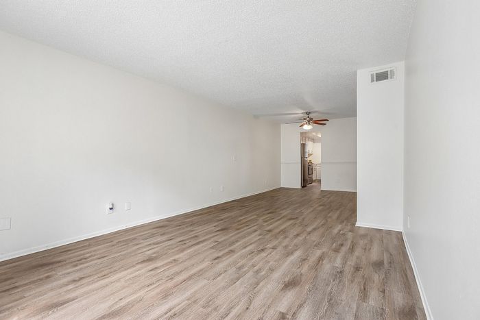 Spacious open-plan living and dining area with elegant wood flooring and modern ceiling fan, seamlessly leading to a bright kitchen.
