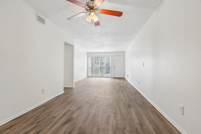 Bright and spacious living room with elegant wood flooring, ceiling fan, and large sliding glass doors opening to a scenic view.
