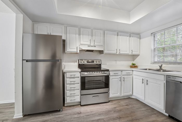 Bright and modern kitchen featuring sleek stainless steel appliances, elegant white cabinetry, and a large window providing natural light.