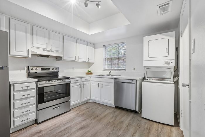 Bright and modern kitchen with sleek stainless steel appliances, abundant white cabinetry, and convenient in-unit laundry.