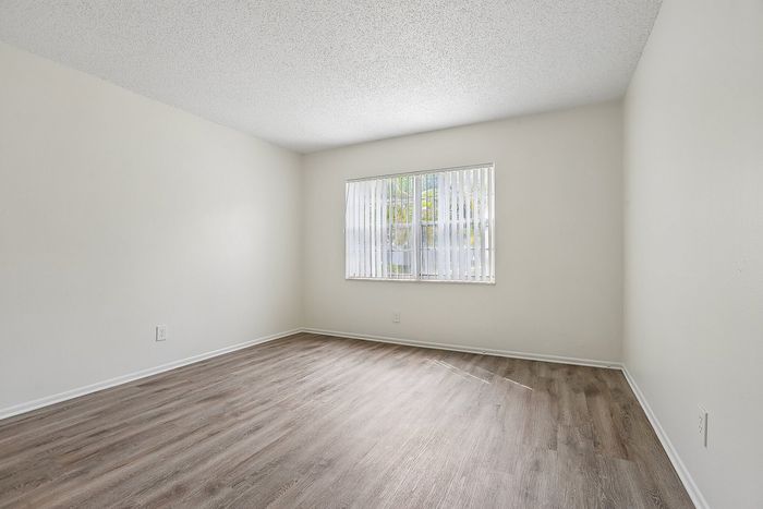 Bright and spacious room featuring elegant wood flooring and natural light from a large window with vertical blinds.