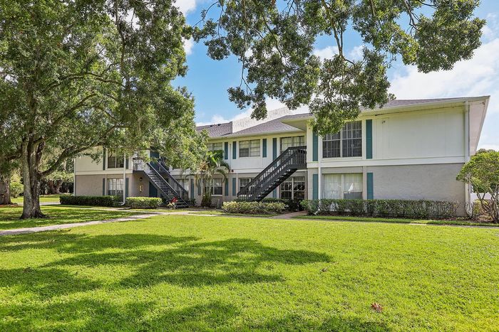 Charming two-story apartment complex surrounded by lush greenery and mature trees, offering a serene and inviting living environment.