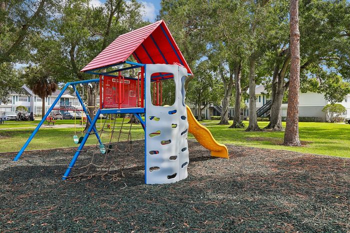 Vibrant playground with a colorful slide and climbing wall, surrounded by lush green trees in a serene residential area.