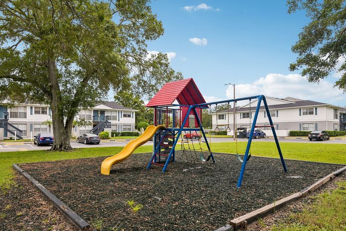Charming neighborhood playground with vibrant playset and swings, nestled among stylish apartment buildings.