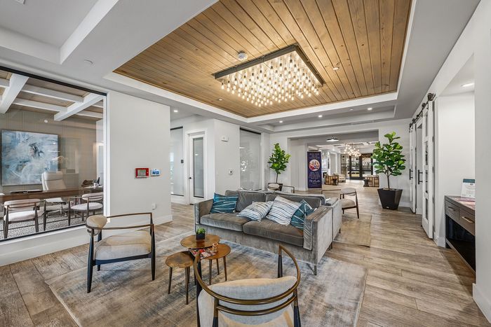 Elegant modern living room with plush gray sofa, stylish armchairs, warm wooden flooring, and an exquisite chandelier, creating a luxurious and inviting ambiance.