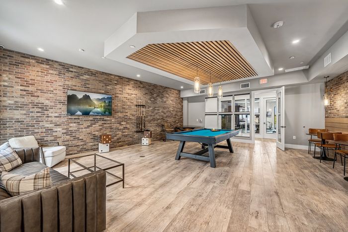 Chic recreational room with modern pool table, stylish brick walls, comfortable seating, and elegant lighting.