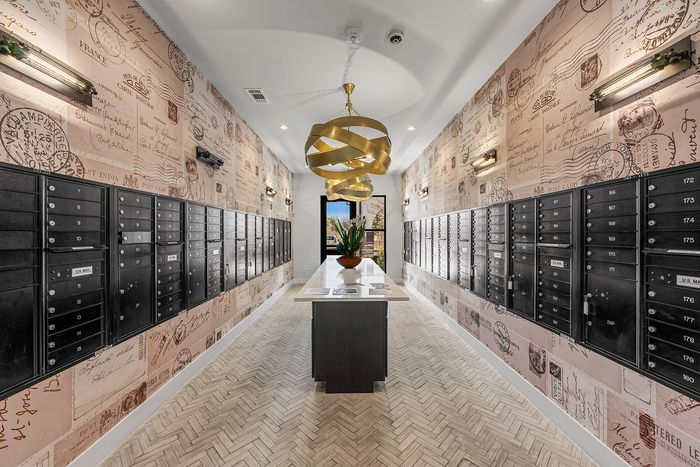 Chic apartment mailroom with stylish vintage postcard wallpaper, elegant lighting, and sleek black mailboxes.