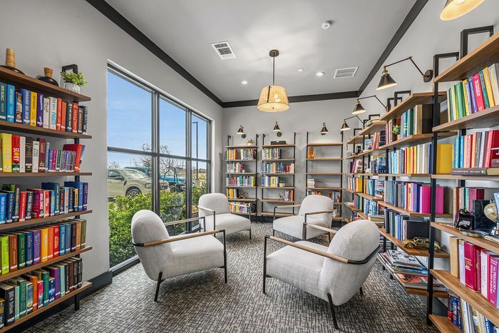 Bright and inviting reading room with contemporary chairs, large windows, and vibrant book-filled shelves, perfect for relaxation and inspiration.