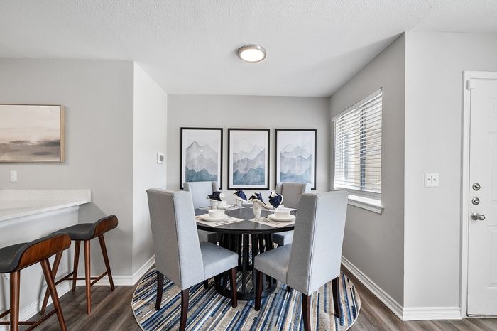 Bright and welcoming dining area with a modern round table and elegant gray chairs, complemented by mountain artwork and large windows.
