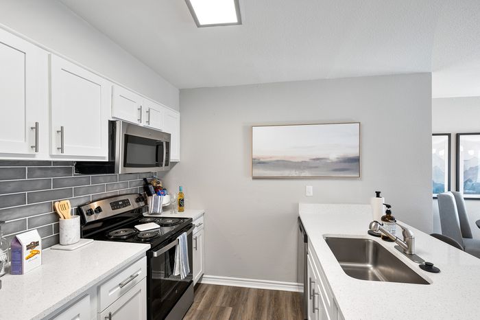 Modern kitchen with sleek white cabinets, high-end stainless steel appliances, and elegant grey backsplash, creating an inviting cooking space.