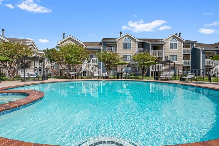Inviting residential complex with a sparkling blue pool, surrounded by elegant multi-story buildings and lush greenery.
