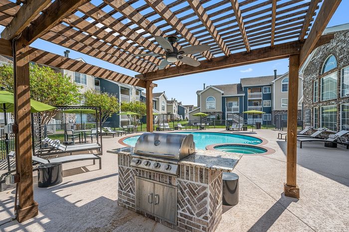 Charming apartment complex showcasing a beautiful pool area with sun loungers, a modern grill under a stylish pergola, and vibrant green umbrellas, perfect for outdoor relaxation.