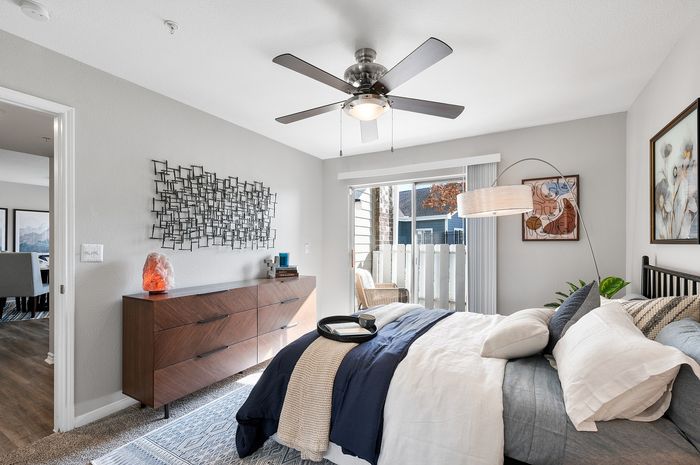 Bright and spacious bedroom with modern decor, featuring a stylish ceiling fan, elegant wall art, and a view of the patio through sliding doors.