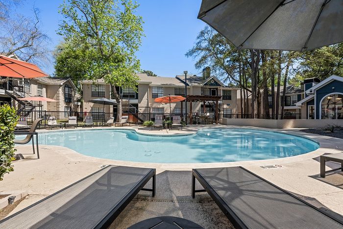 Inviting apartment complex pool area with sun loungers, umbrellas, and lush greenery, ideal for relaxation and leisure.